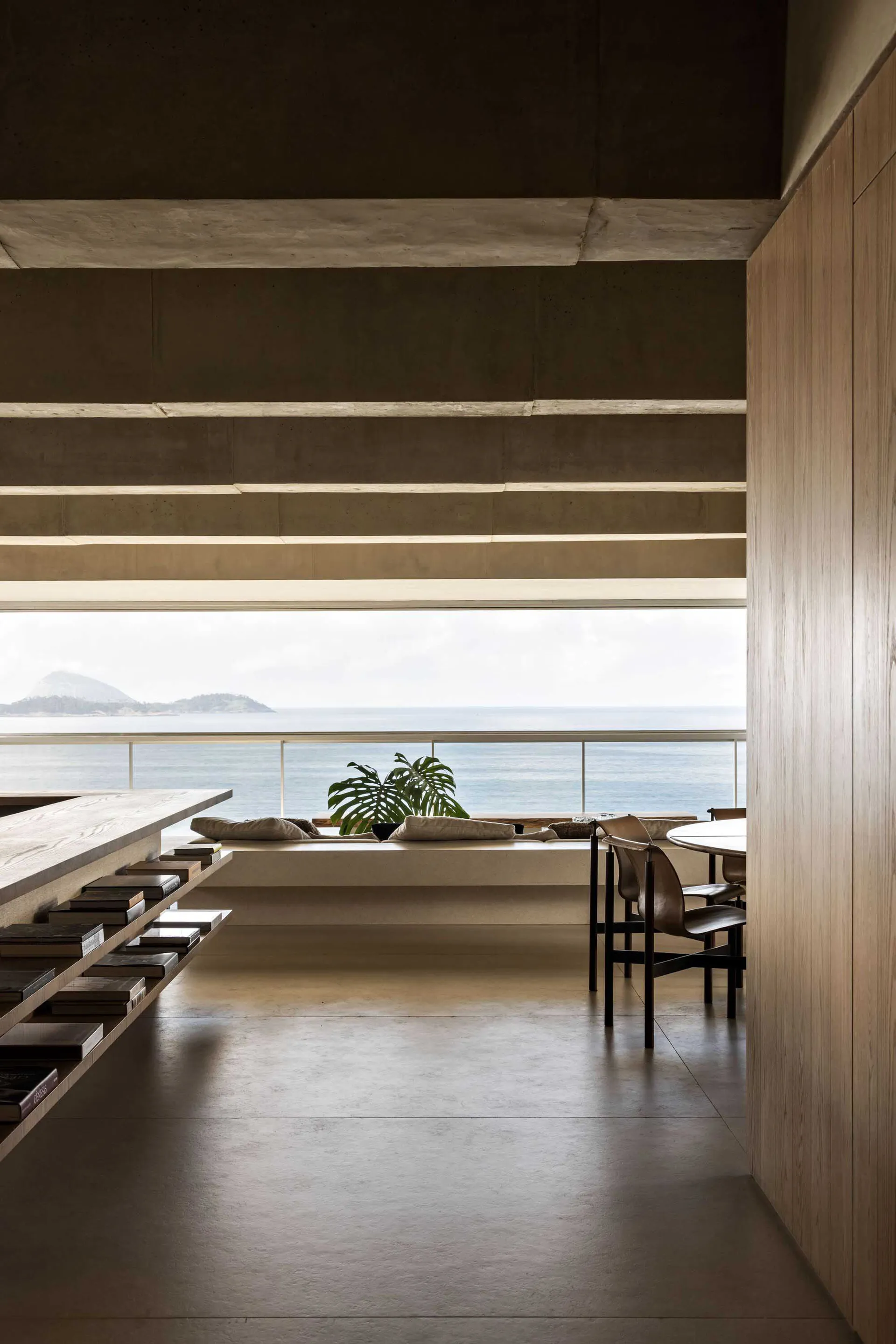 A modern home interior featuring concrete walls and wooden furniture with a view of the sea.