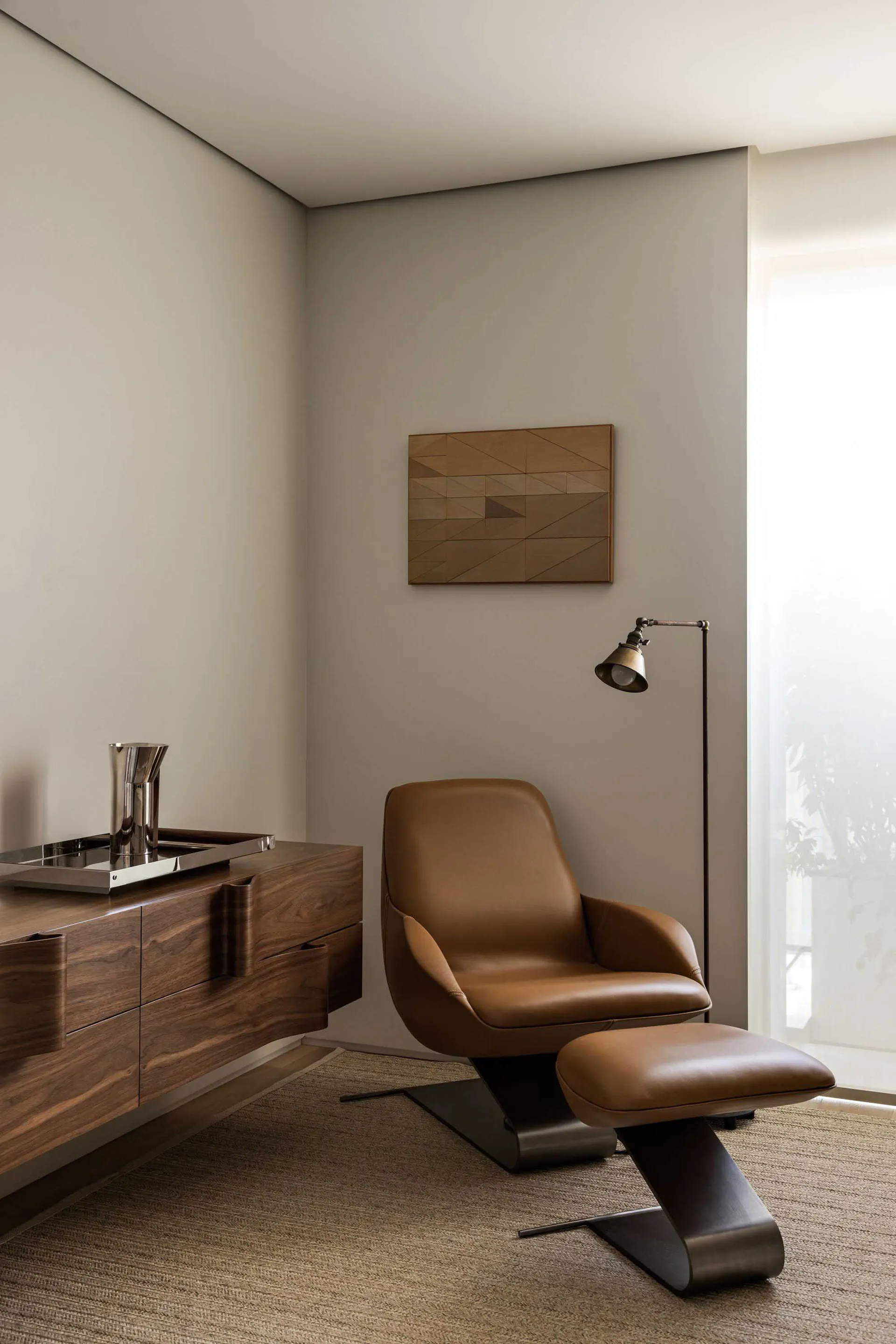 Modern living room with a brown leather armchair and metallic floor lamp, featuring a geometric wall art.