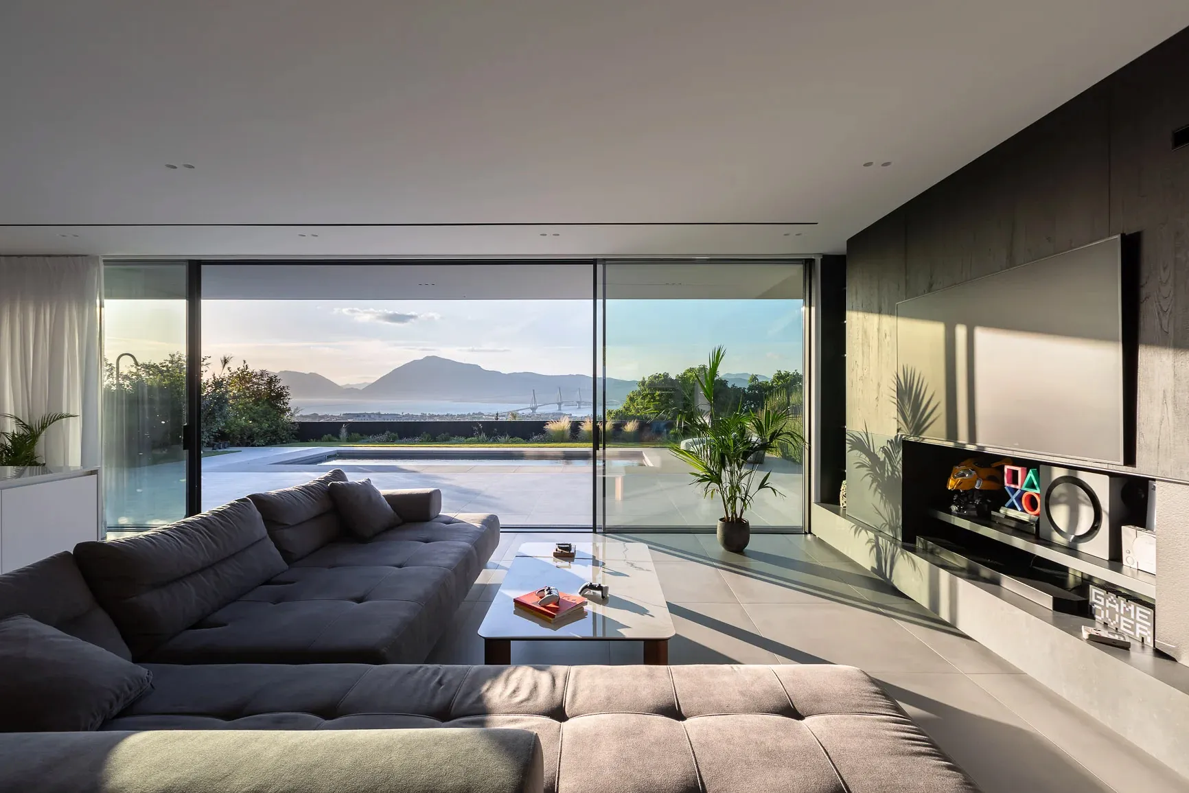 A modern minimalist living room with large glass walls and concrete flooring, featuring a spacious sofa and a sleek, minimali