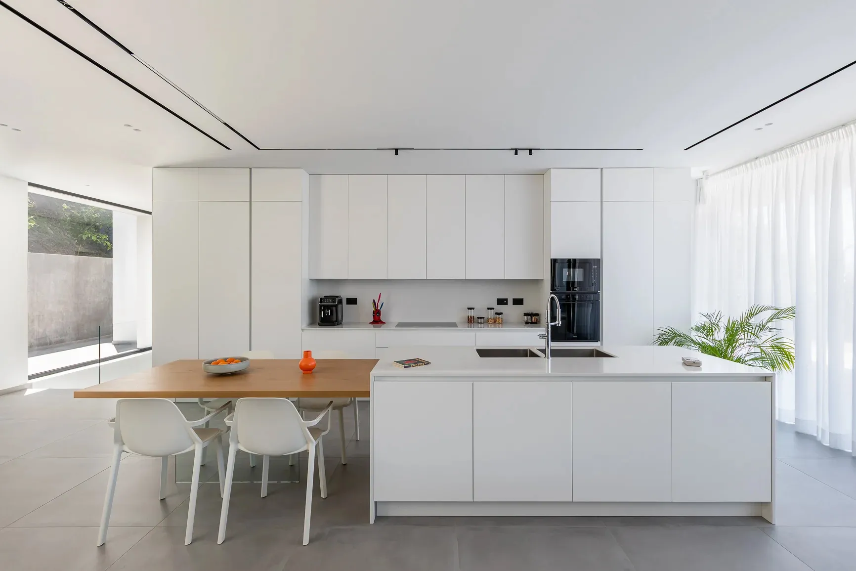 A modern kitchen with white concrete walls and white cabinets, featuring a large island with a wooden countertop.
