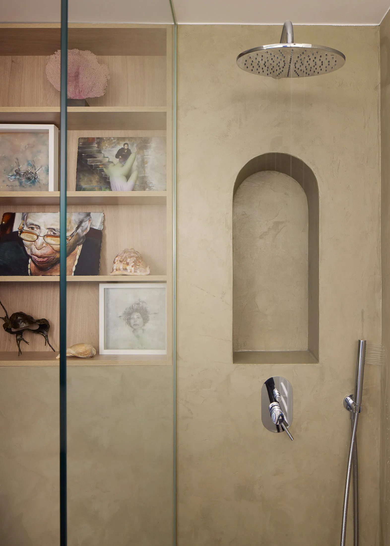 A minimalist bathroom with concrete walls and shelves containing various artworks and seashells.