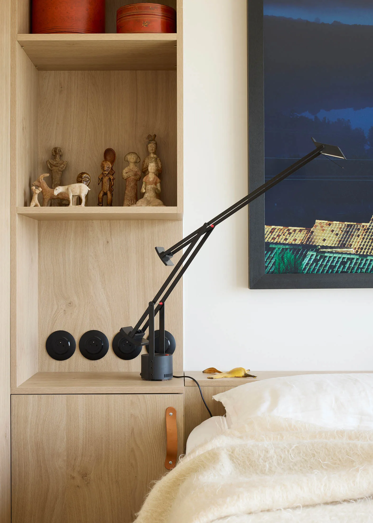 A minimalist bedroom with a modern desk lamp and wooden shelves.