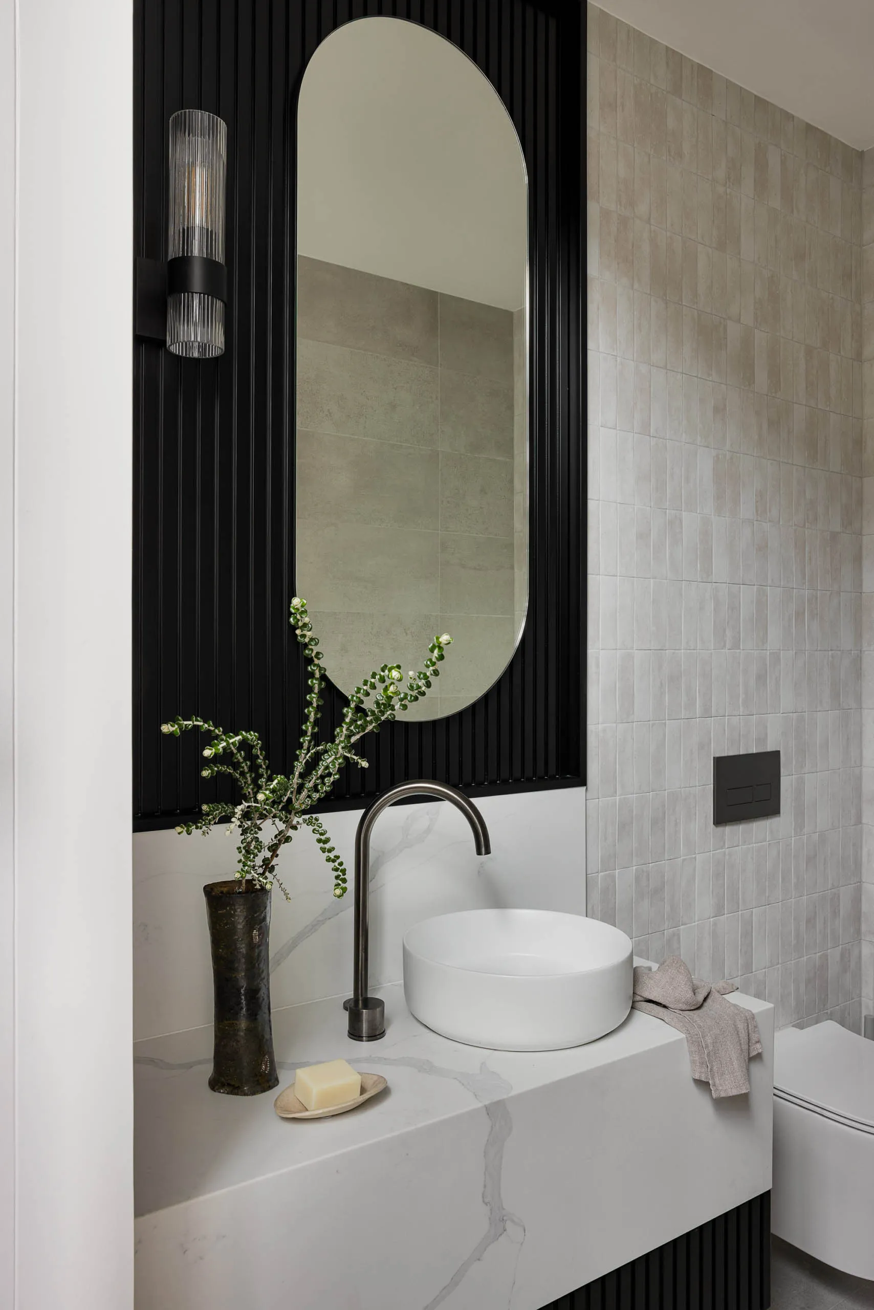 A modern bathroom featuring a marble sink with a round basin and a sleek faucet. Decorative elements include a vase with gree