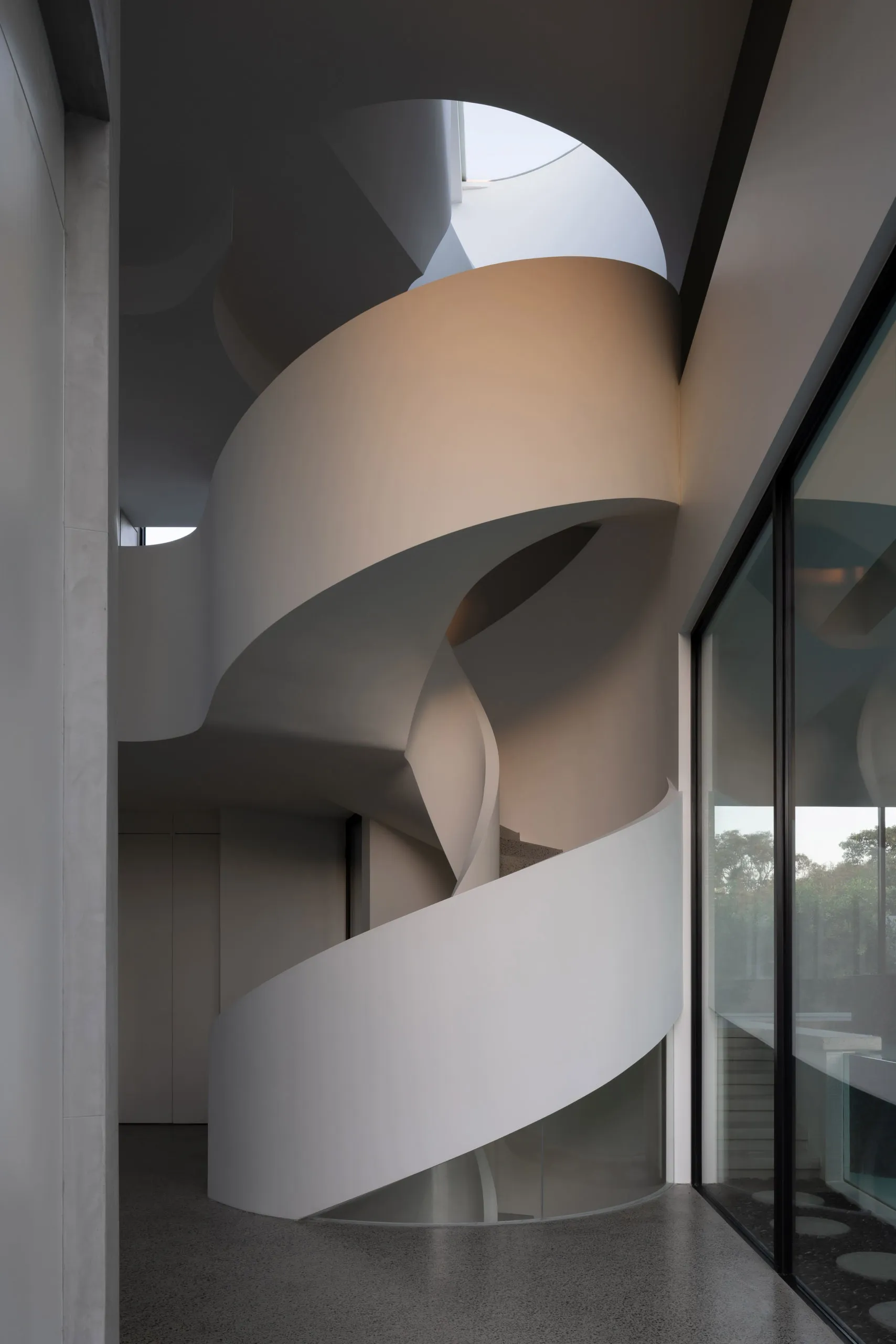 Modern interior design featuring a concrete spiral staircase with natural light.