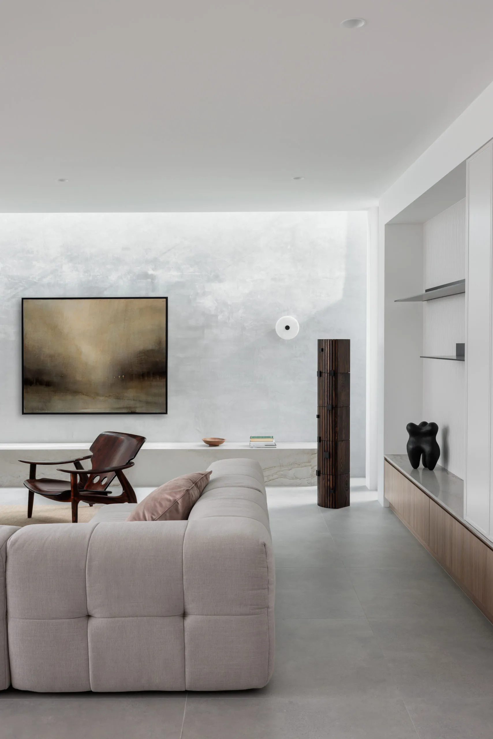 A modern interior design of a living room featuring a concrete wall, minimalist furniture, and abstract art.