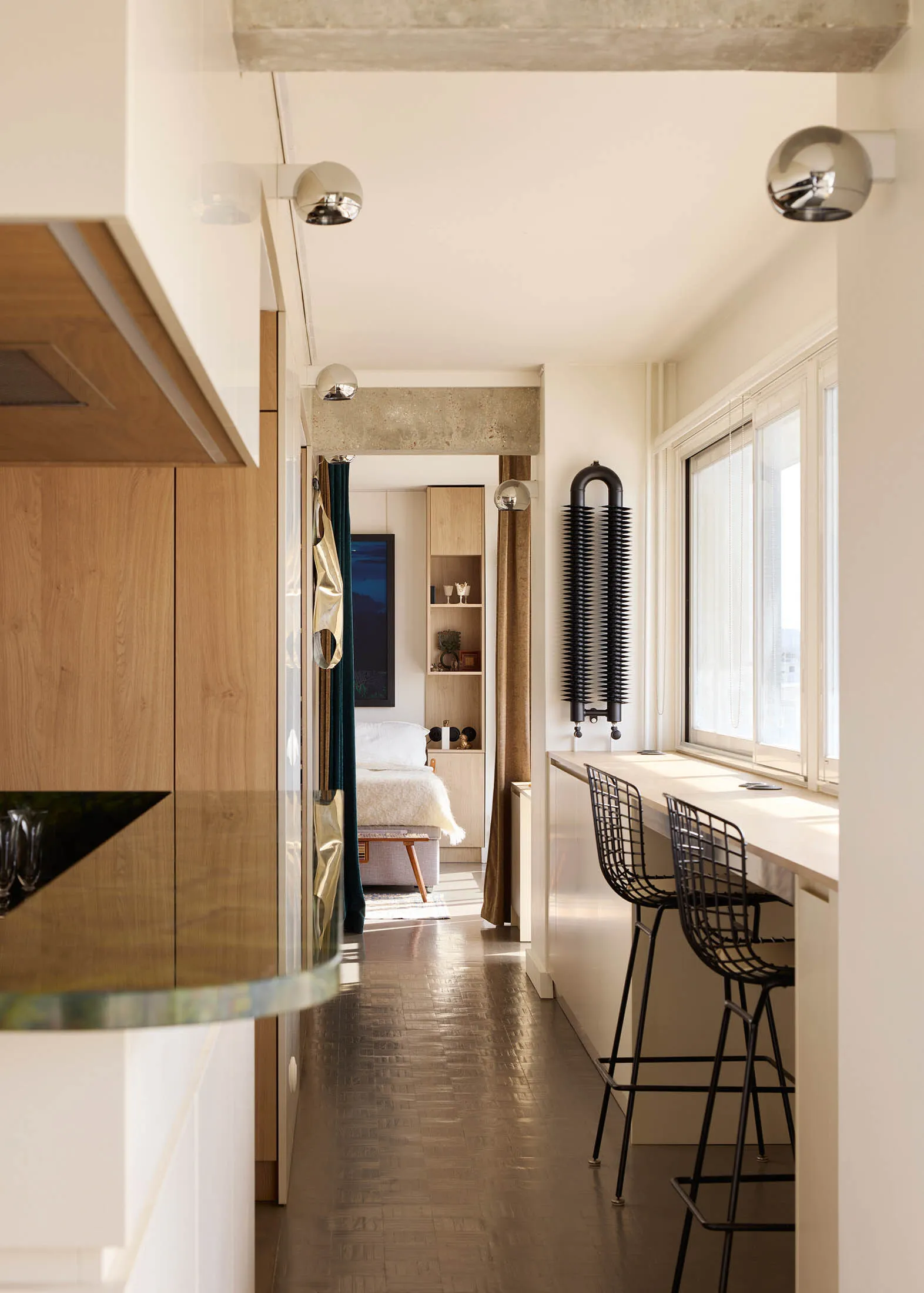 A modern minimalist kitchen bar area with wooden cabinets, glass countertops, and metal stools.