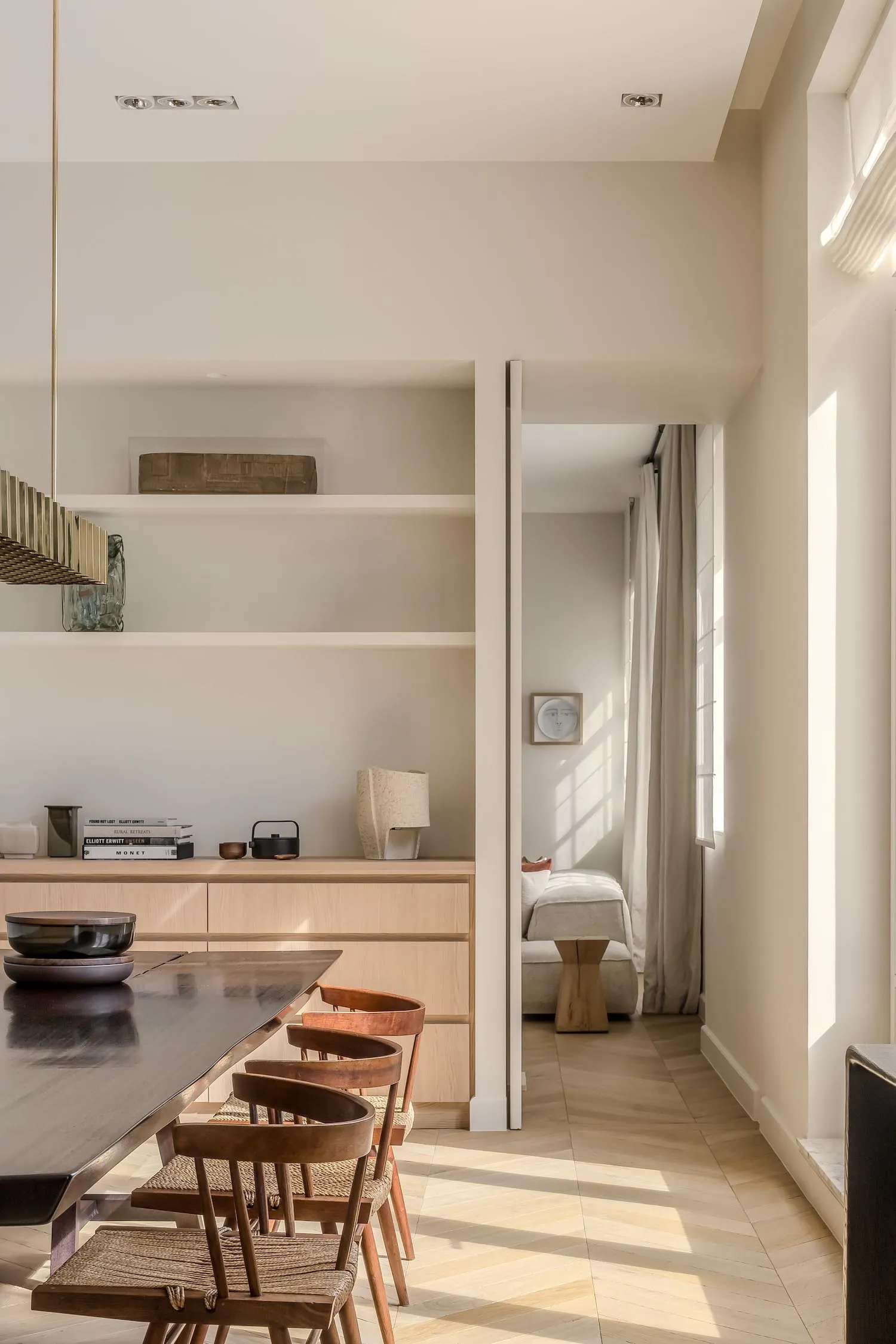 Modern minimalist dining room featuring a wooden table, chairs, and shelving unit with books and decorative items.