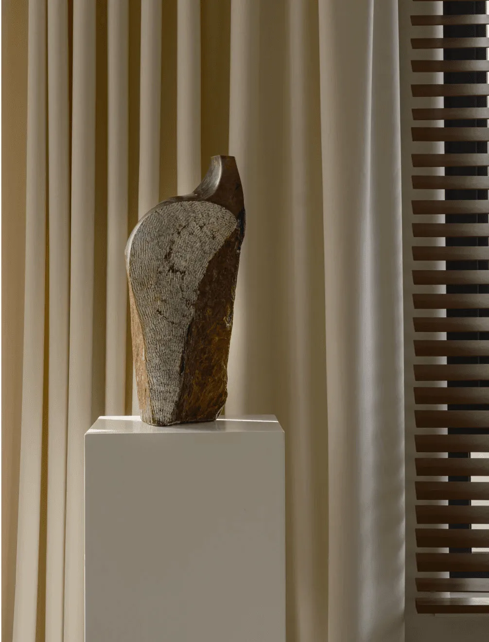A minimalist stone sculpture on a pedestal in a modern interior setting
