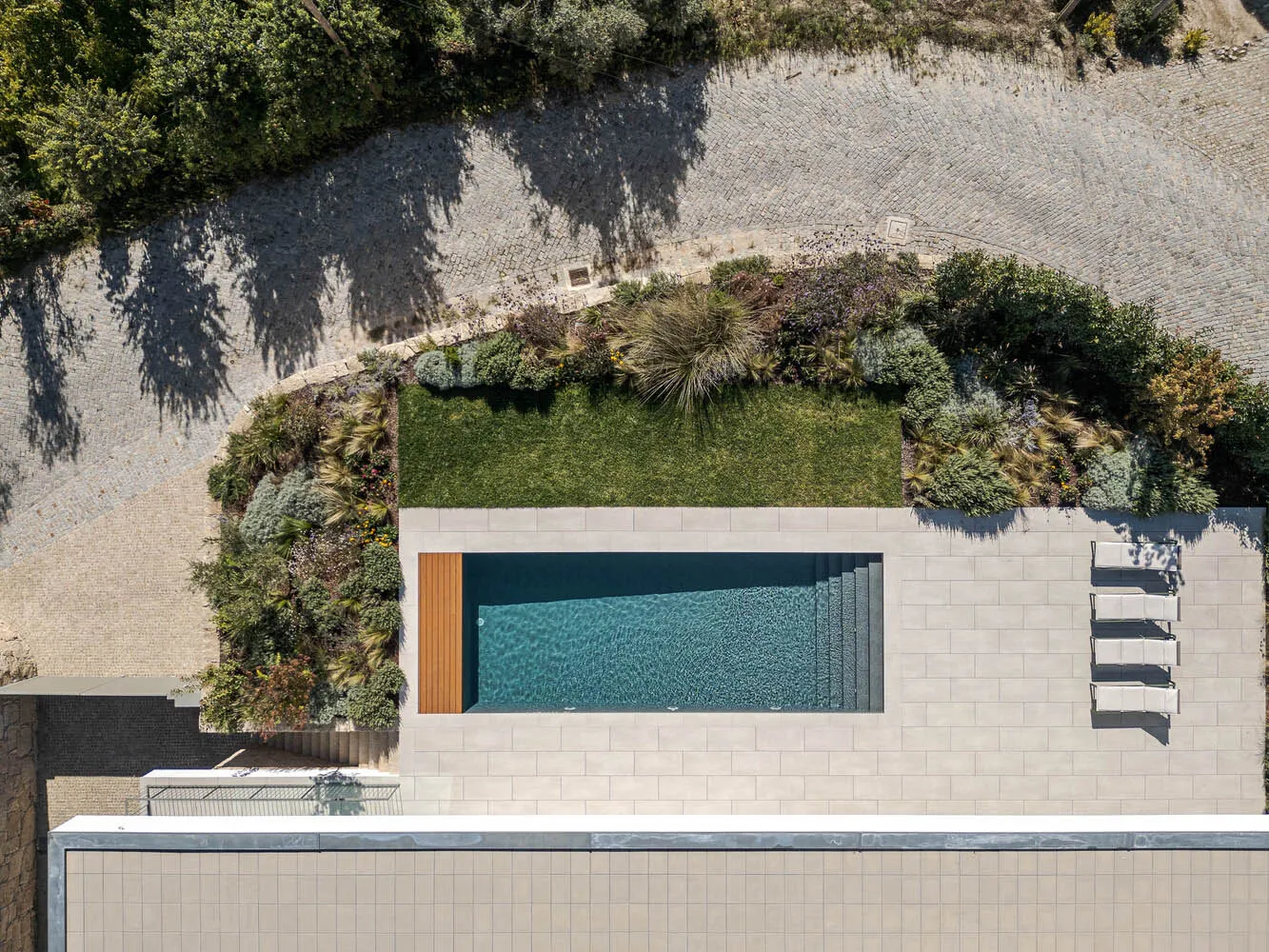Aerial view of a modern residential pool with concrete patio and surrounding garden.