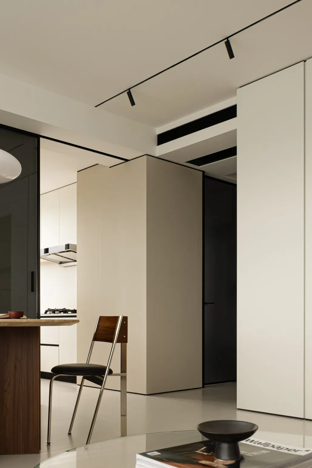 A modern minimalist living room with a concrete open-plan design, featuring a sleek wooden dining table and a black chair.
