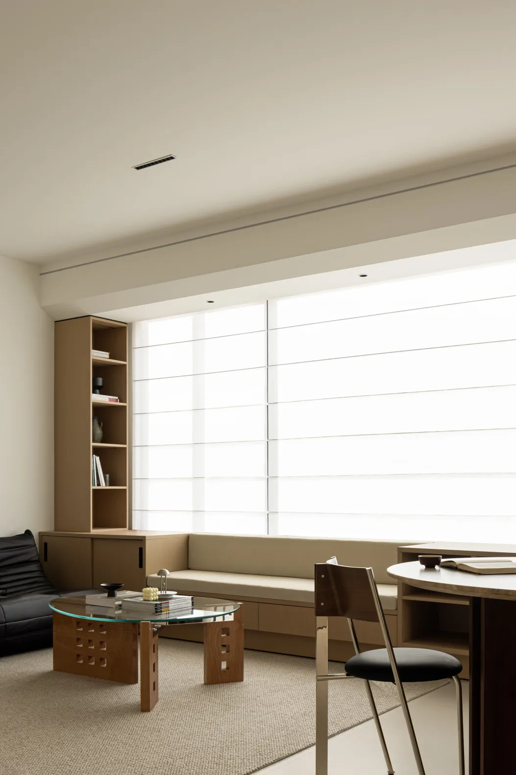 A minimalist living room with wooden furniture, white walls, and a sleek table with books and a lamp.