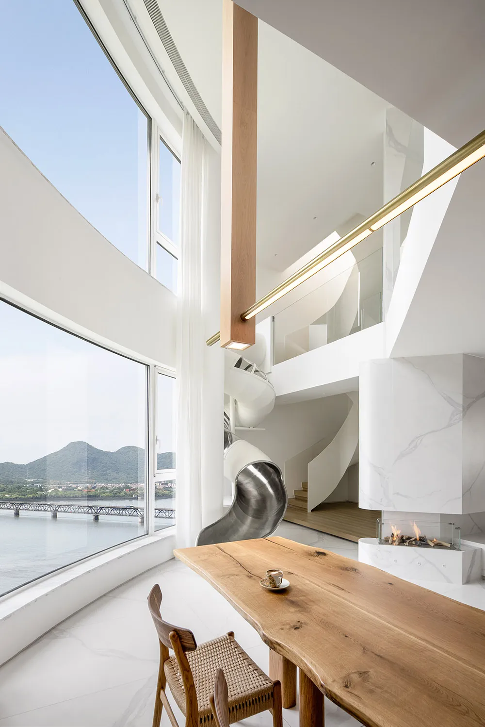A modern minimalist kitchen featuring a spacious dining area with a wooden table and chairs, floor-to-ceiling windows overloo