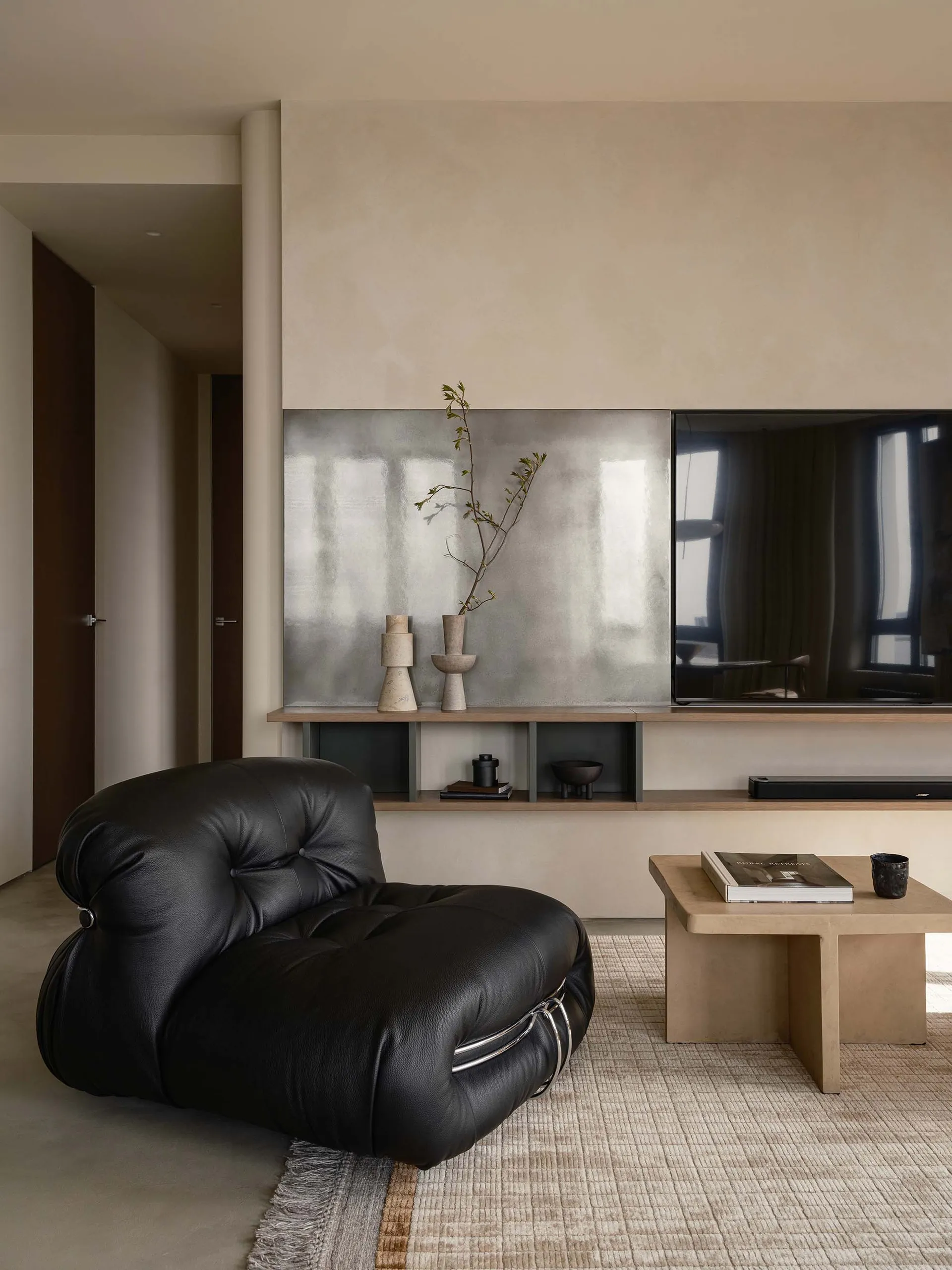 A modern minimalist living room featuring a black leather armchair, a concrete floor, and a concrete wall panel with a flat-s
