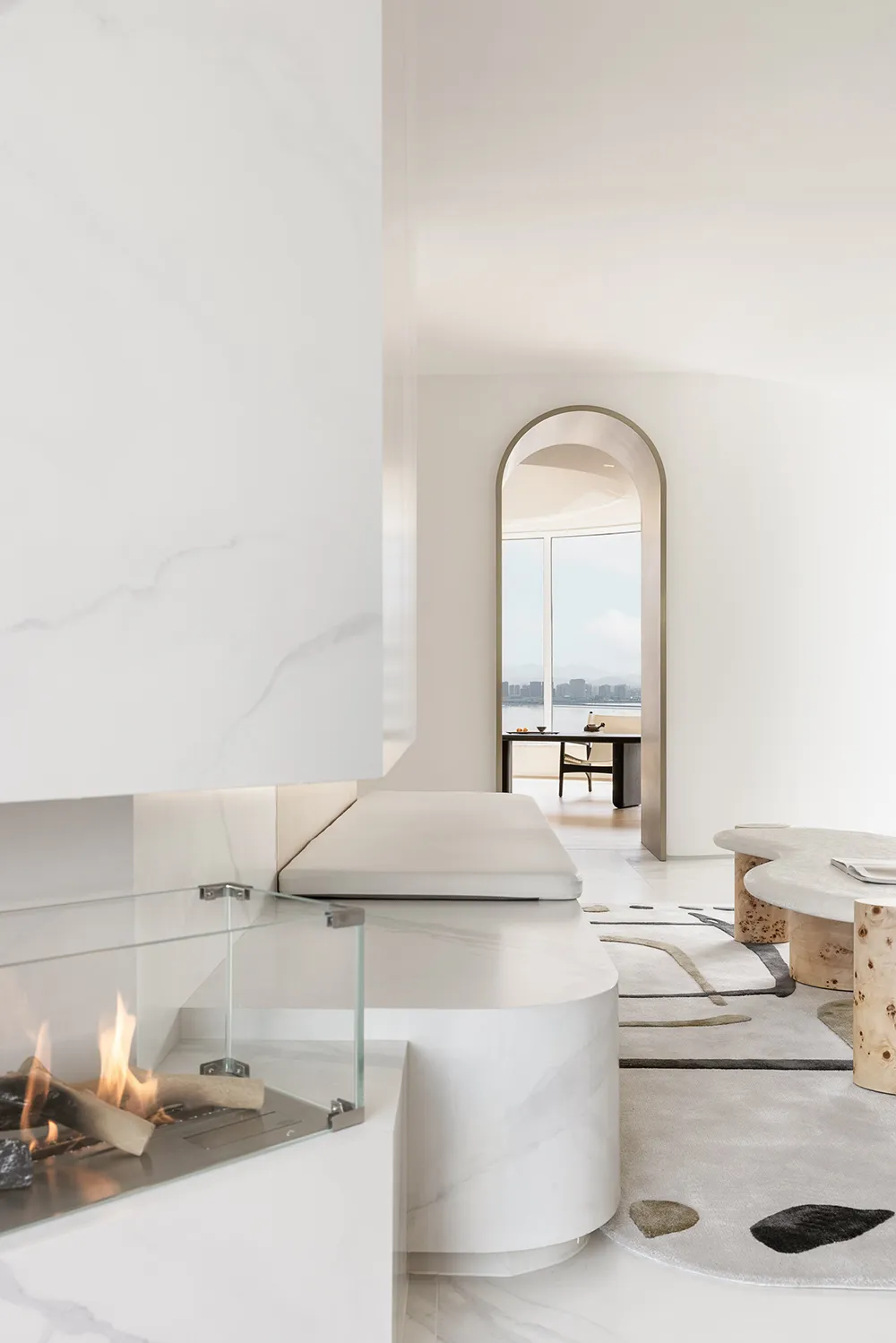 Modern minimalist living room featuring marble fireplace and furniture, with a view of a cityscape through an archway.