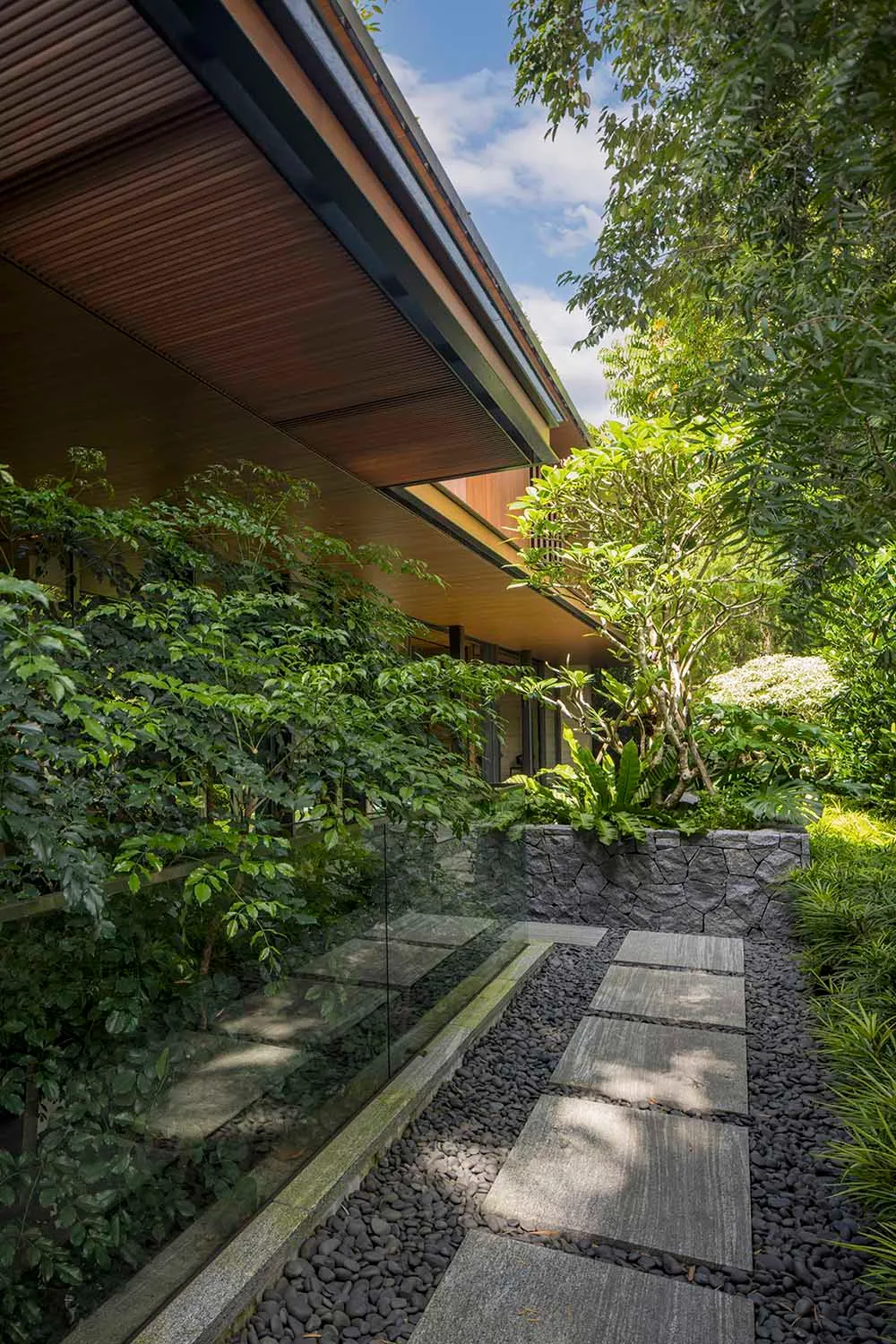 Modern garden with a stone pathway bordered by small rocks and lush greenery.