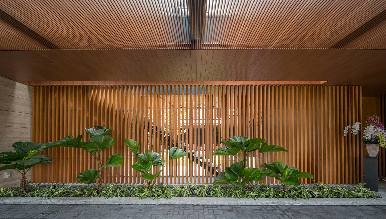 A modern entrance with a wooden slat wall and green plants in front of it.