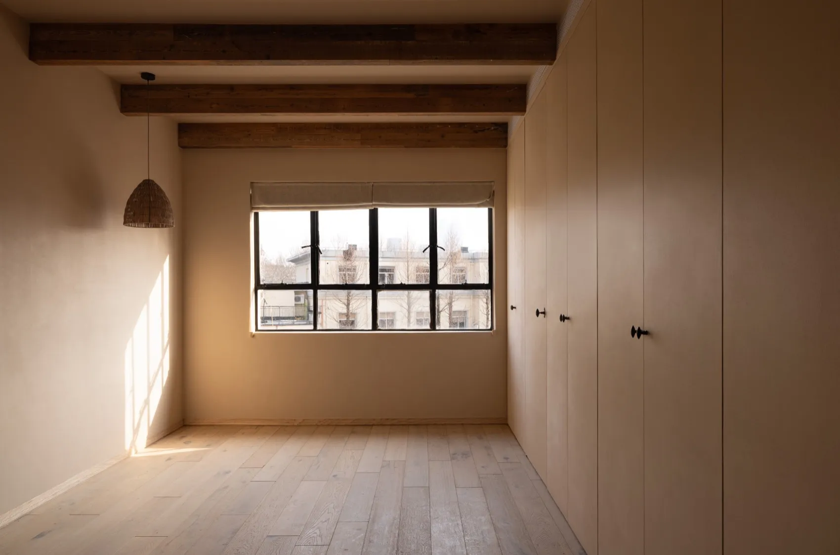 An empty minimalist room with wooden floors, a large window, and wooden beams.