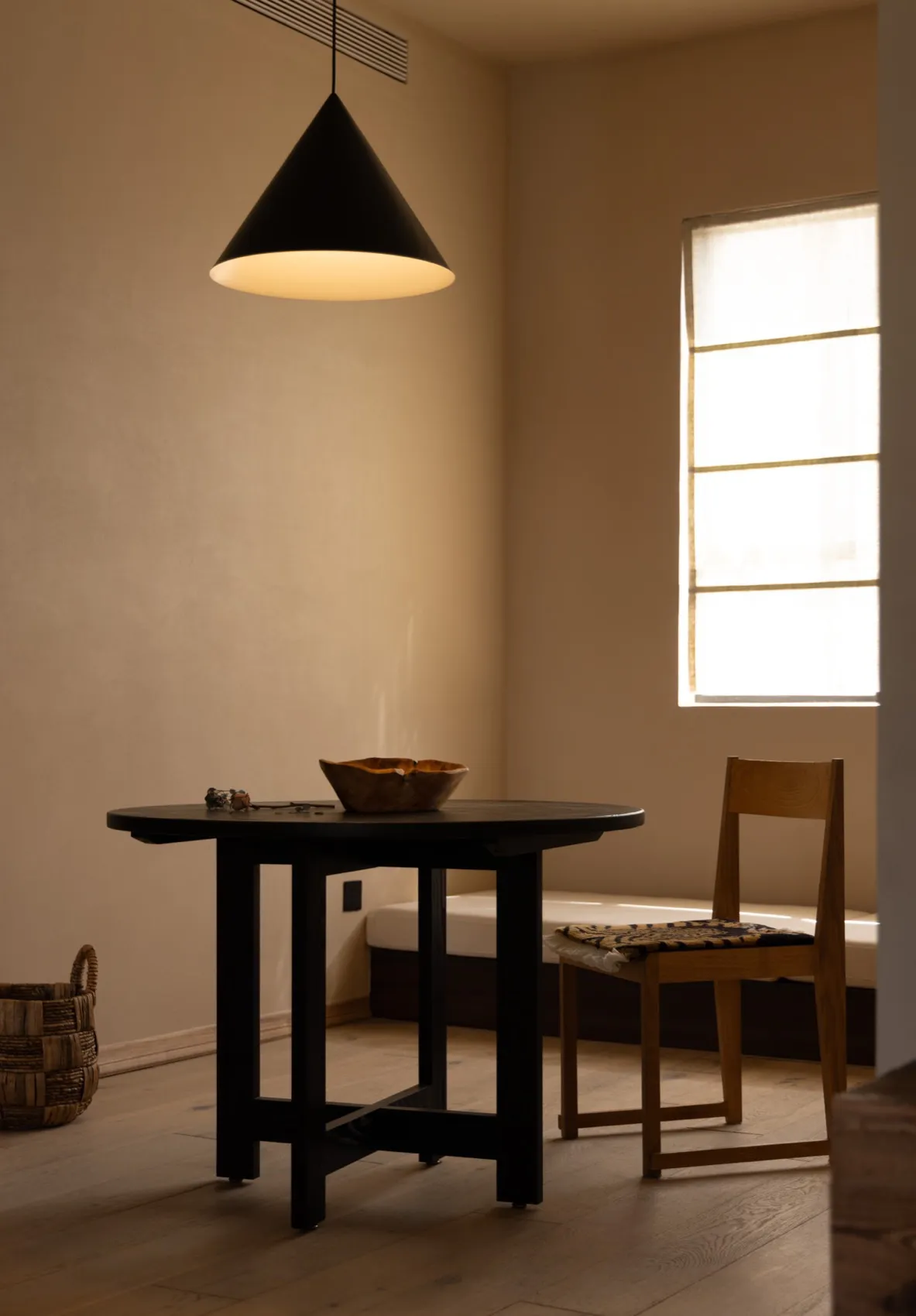 Minimalist interior design featuring a simple wooden table with a bowl on top, a wooden chair, and a window letting in natura