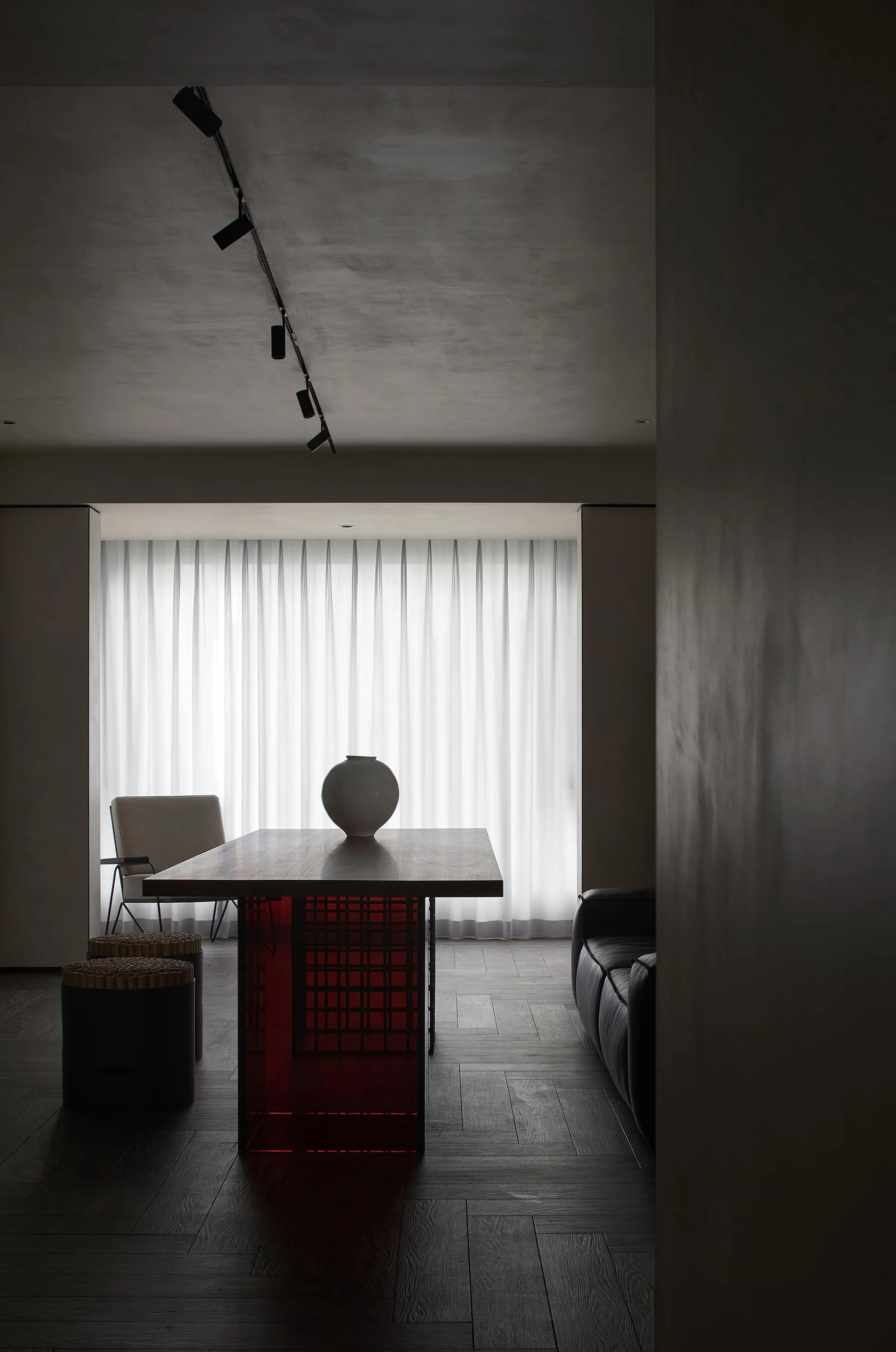 A modern living room with a wooden floor, red table legs, and a white vase on the table.