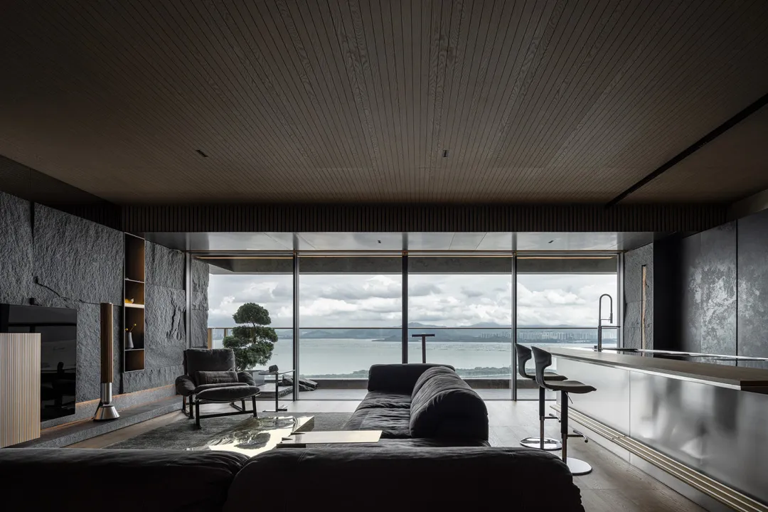 A modern minimalist living room featuring a concrete couch and glass walls overlooking a scenic view of the sea.