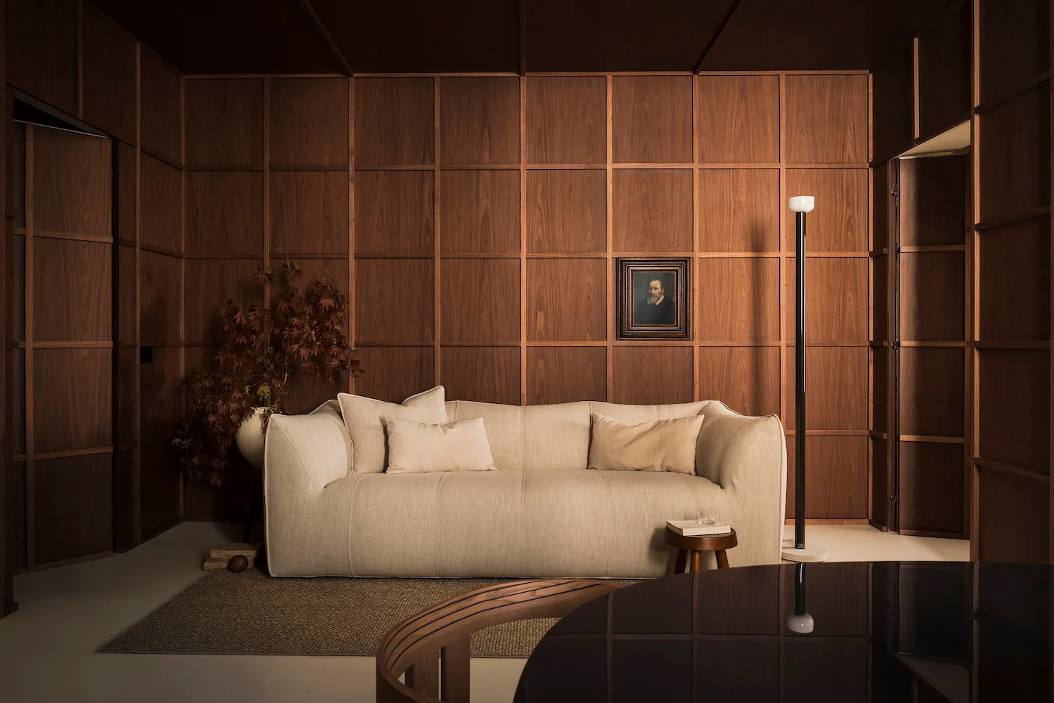 A cozy living room featuring a beige sofa, wooden panel walls, and a framed portrait.