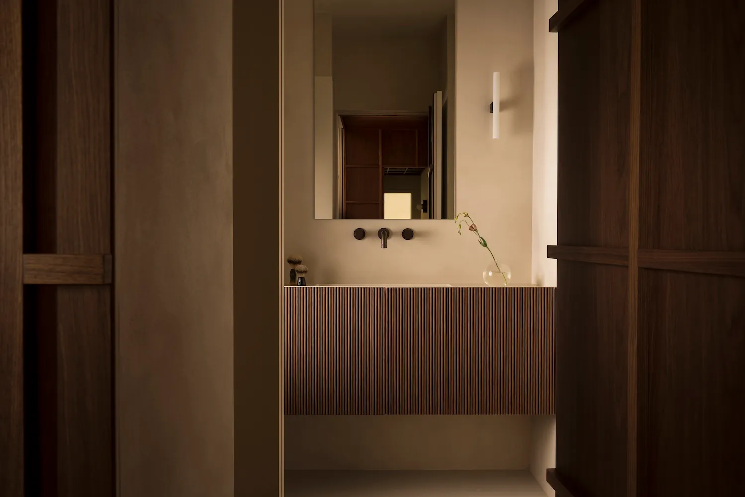 A minimalist bathroom with a wooden vanity and ceramic sink.