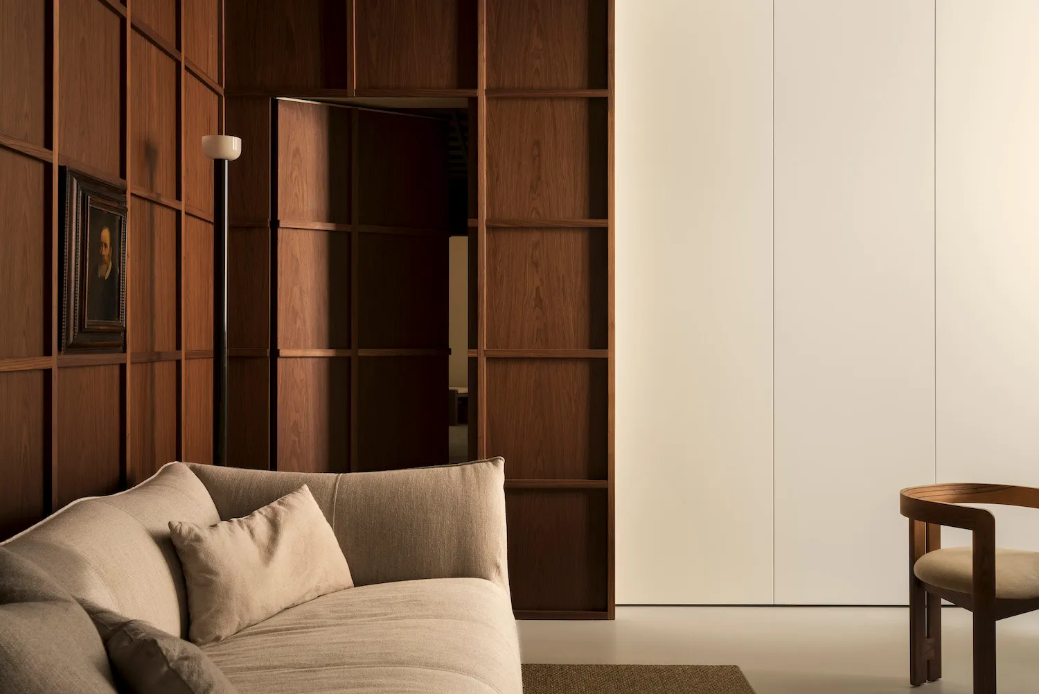 Modern minimalist living room with wooden paneled walls and a beige upholstered sofa.