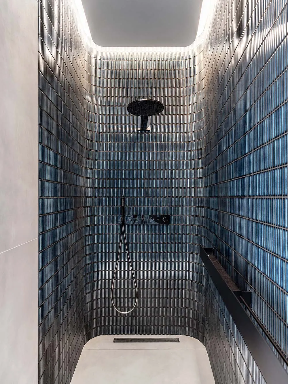 A minimalist bathroom with glass tiles, featuring a shower area with a ceiling light and a hand-held showerhead.
