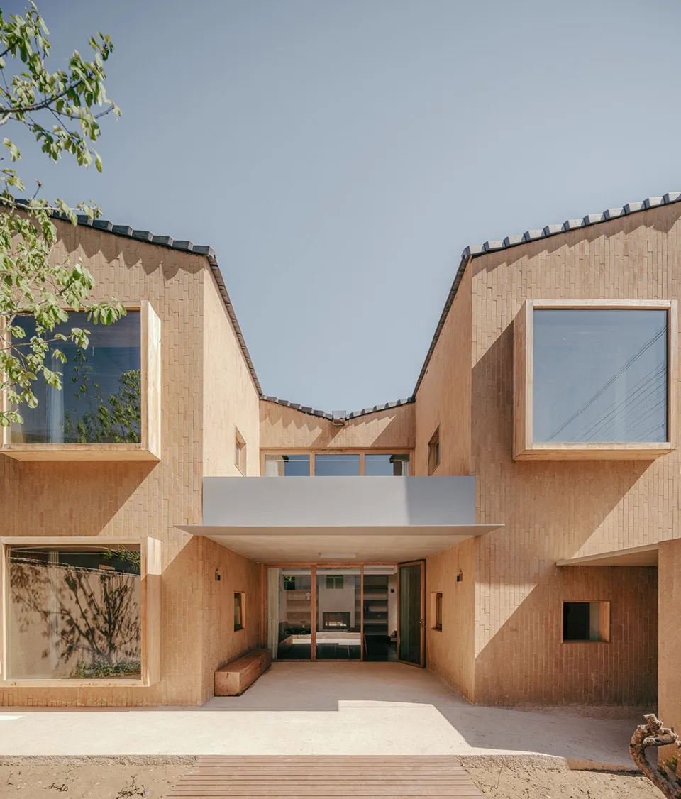 A modern building facade made of clay with large windows and a concrete awning.