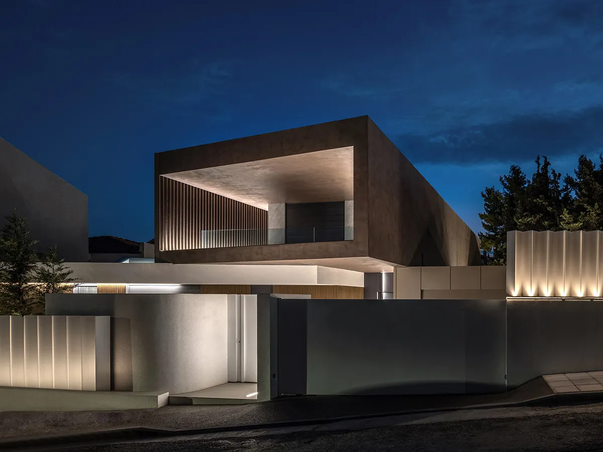 A modern building exterior with concrete walls and glazed tiled sections illuminated at night.