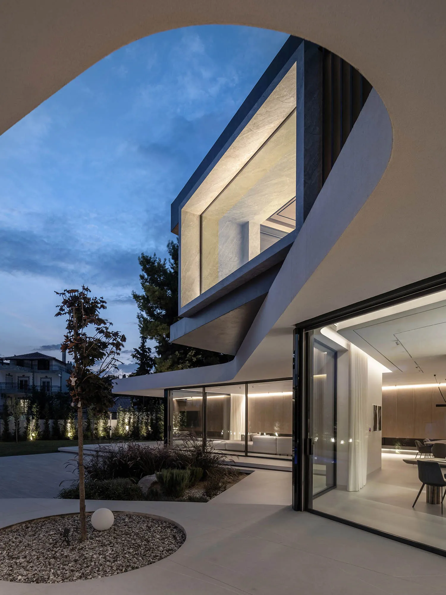 A modern house exterior at night with illuminated interiors and a landscaped garden.