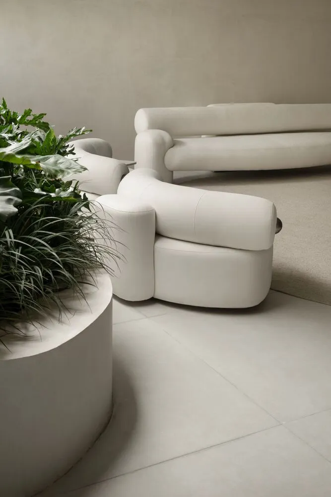 A modern white sofa with circular base and a matching white circular planter with green plants next to it.