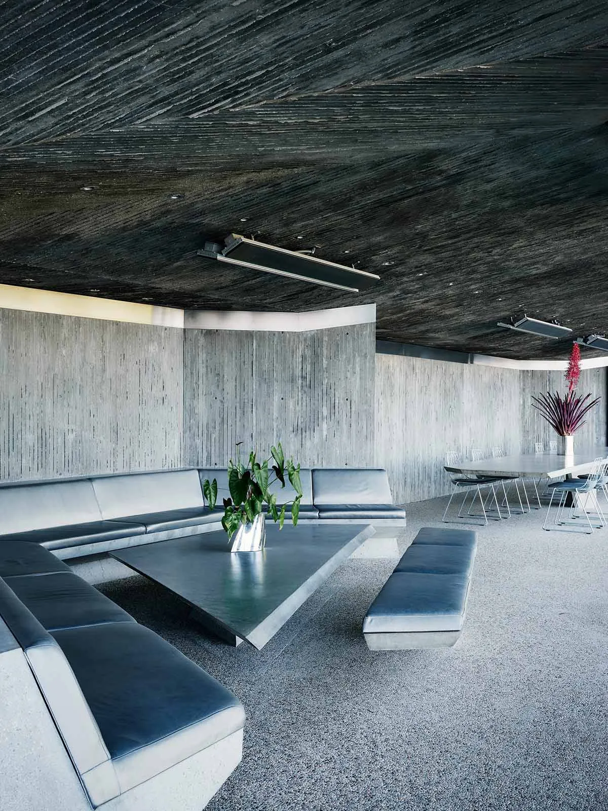 Modern lobby space with a concrete ceiling, floor, and walls featuring a triangular coffee table and seating areas.