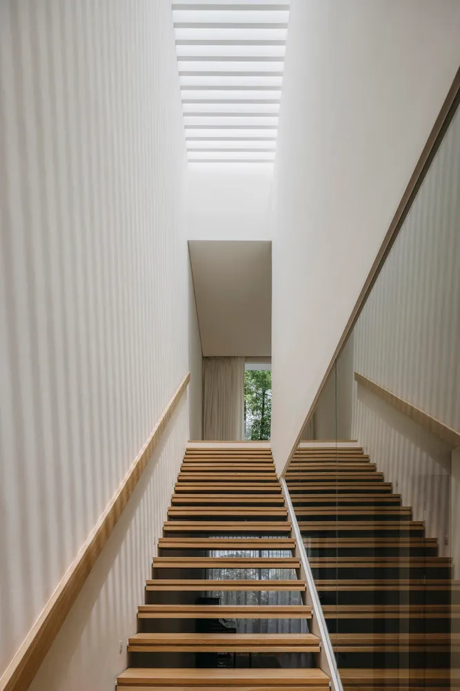 Modern minimalist staircase made of light-colored wood with a glass wall and a wooden handrail.