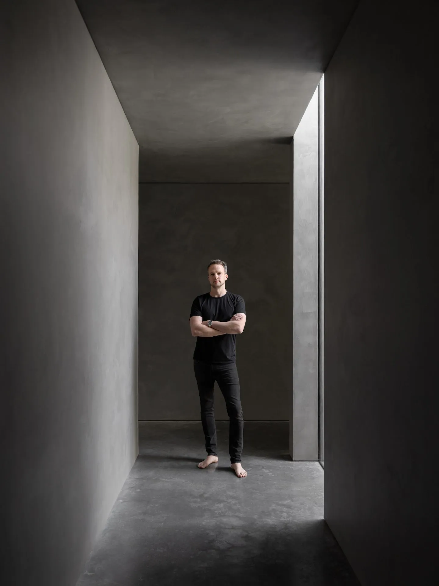 A minimalist interior with concrete walls and flooring in a narrow, well-lit corridor.