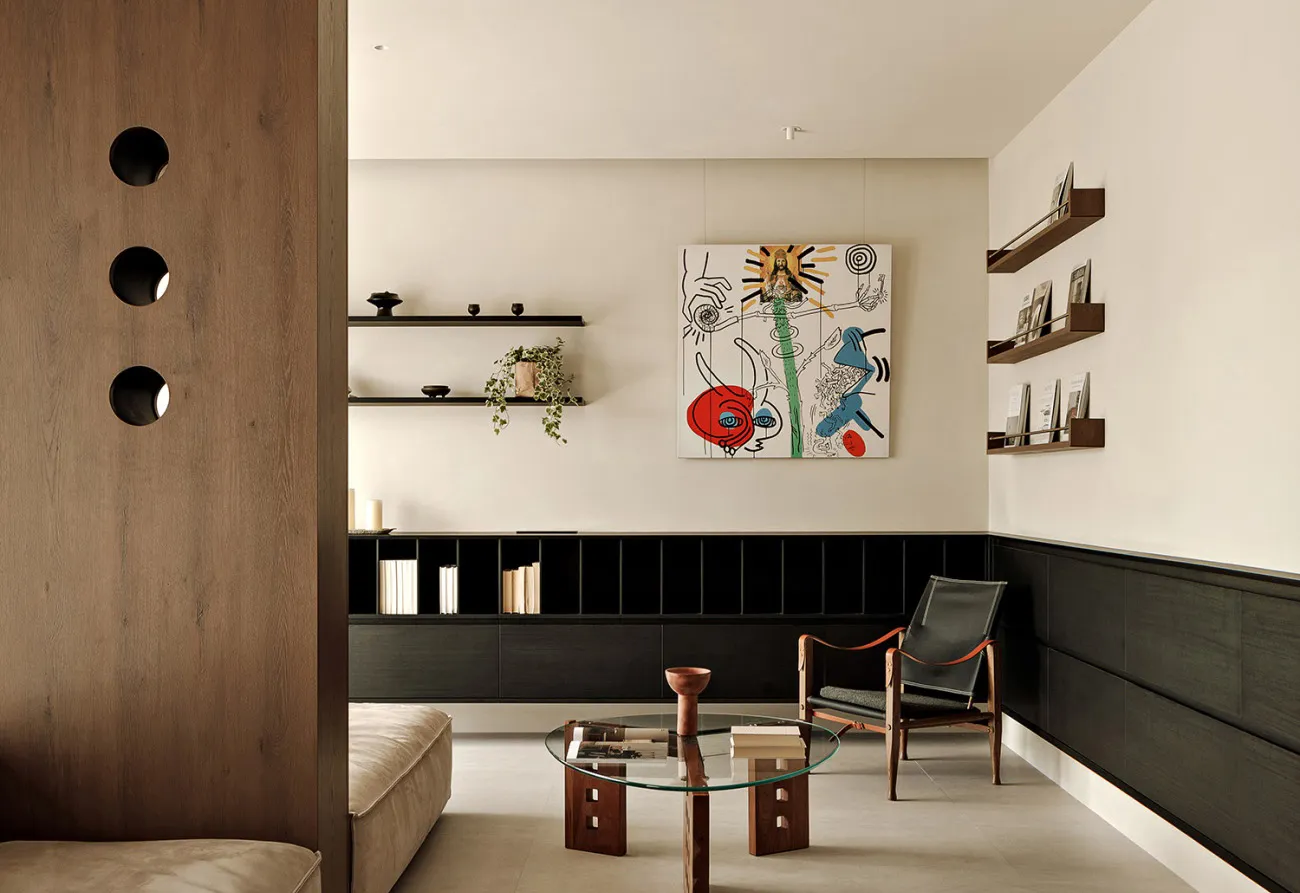 A minimalist living room with wood accents, glass coffee table, and metal-frame chair.