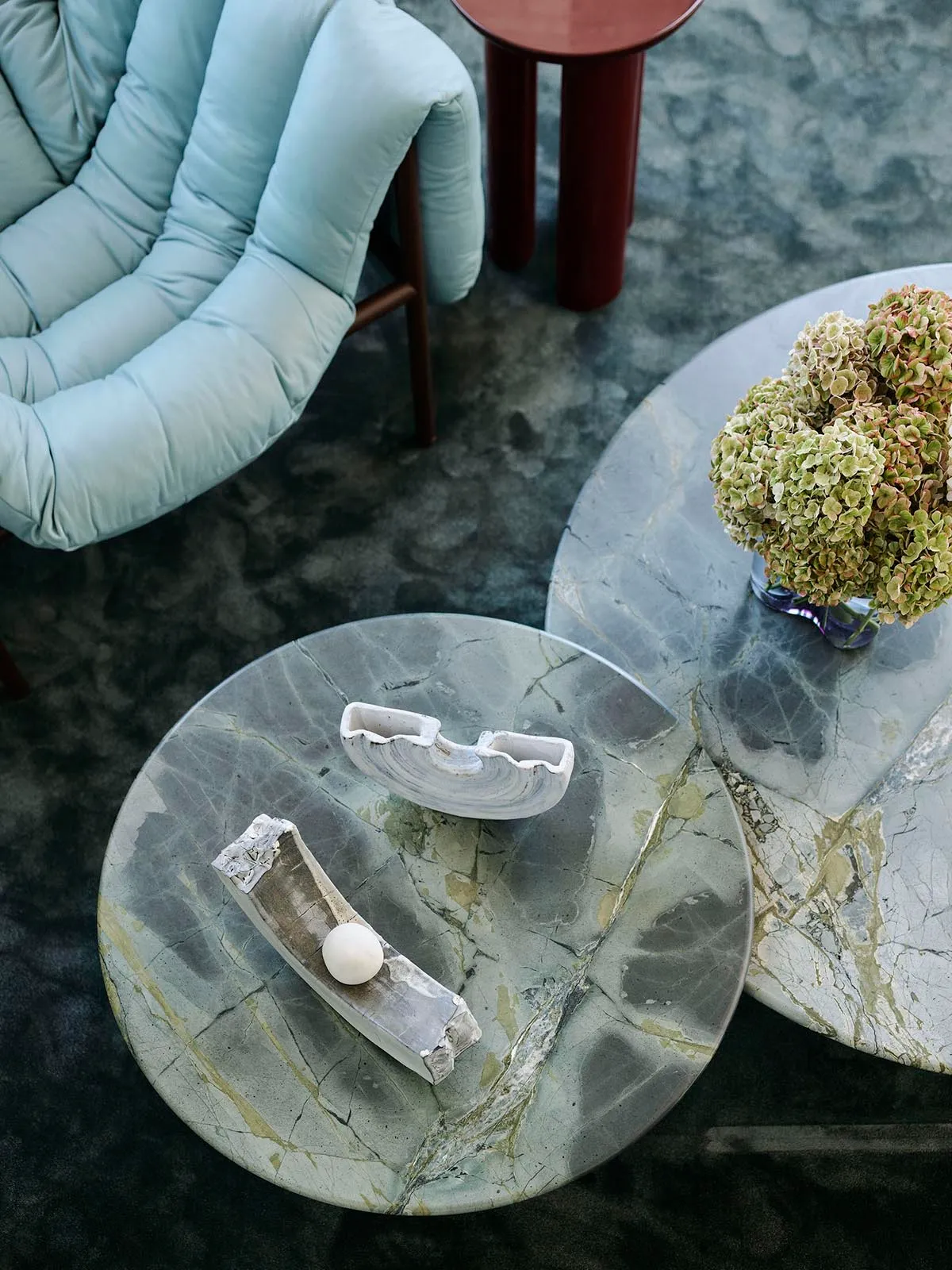 A modern living room featuring marble tables with decorative concrete sculptures and a vase of hydrangeas.