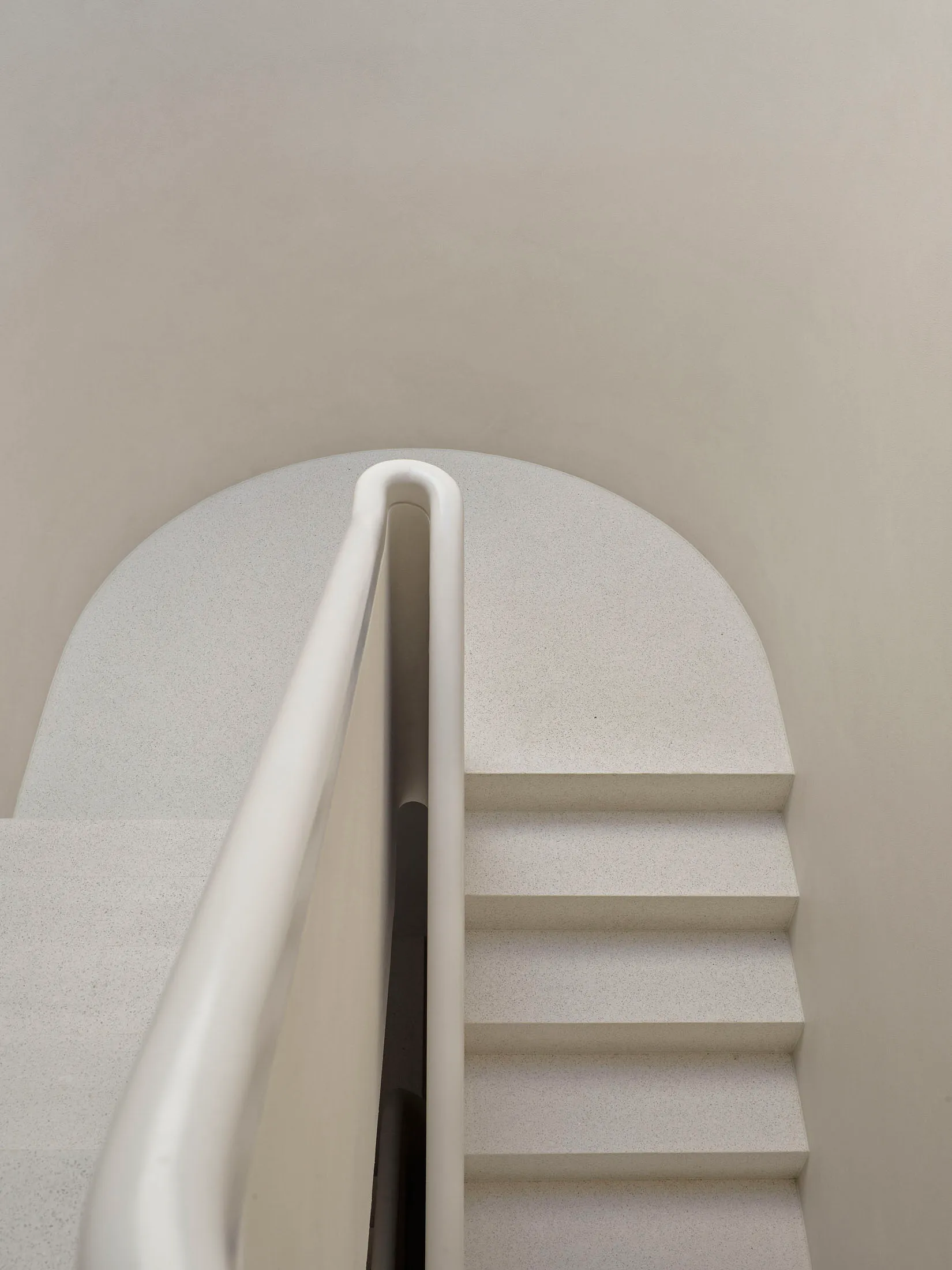 A minimalist concrete staircase with a white curved handrail.