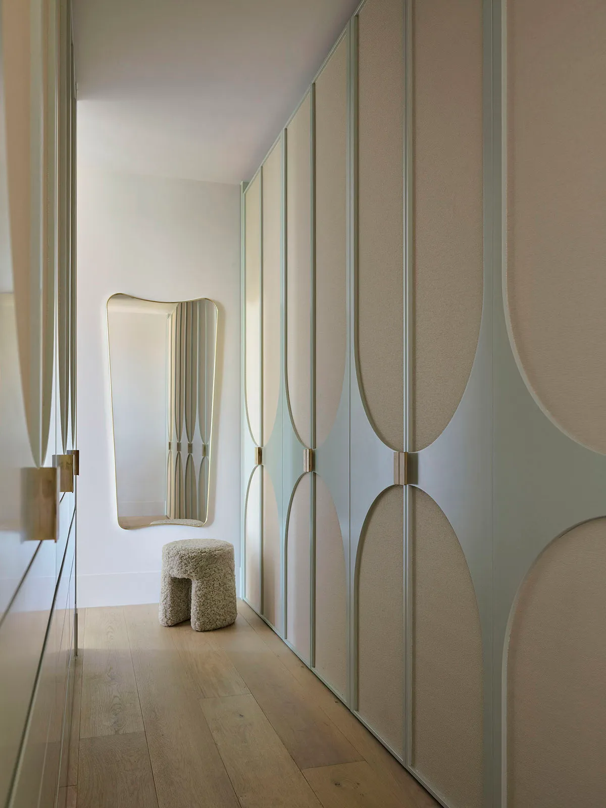 Modern closet with linen fabric wall covering, circular door designs, and a stool with a textured surface.