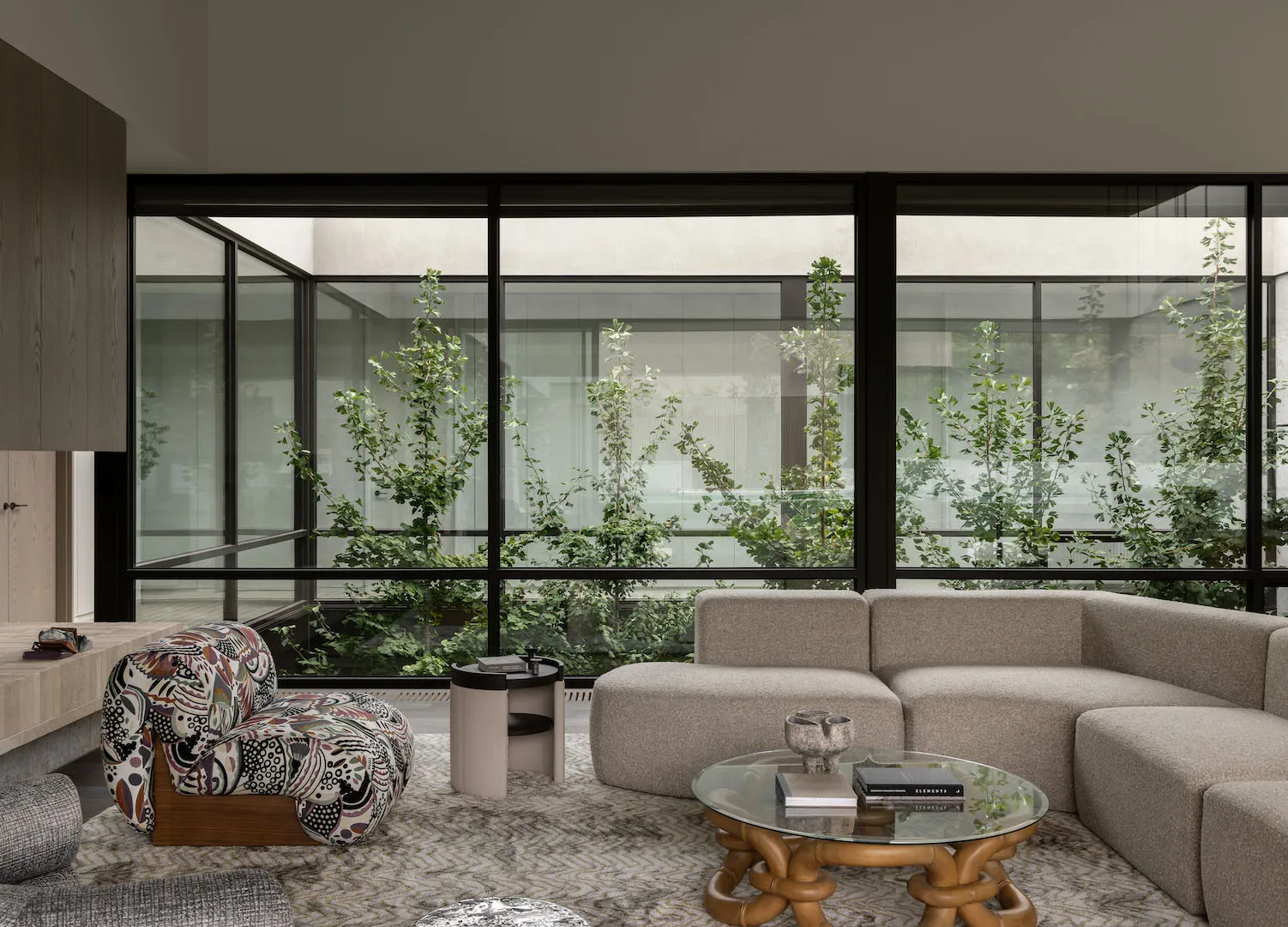 A modern minimalist living room with a large glass wall, neutral textiles, and greenery.