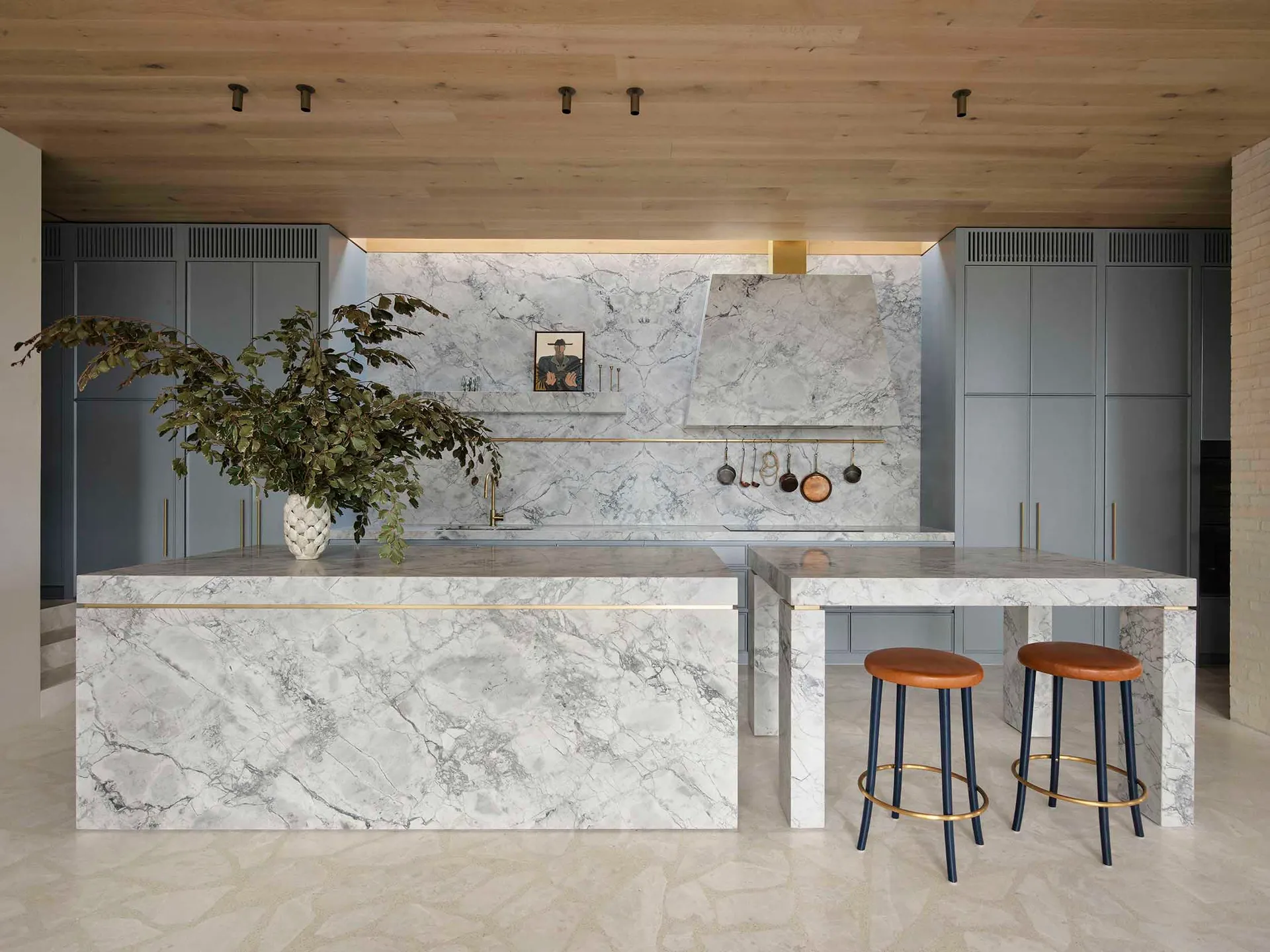 Modern residential kitchen featuring a large marble island with a vase of greenery and stools underneath.