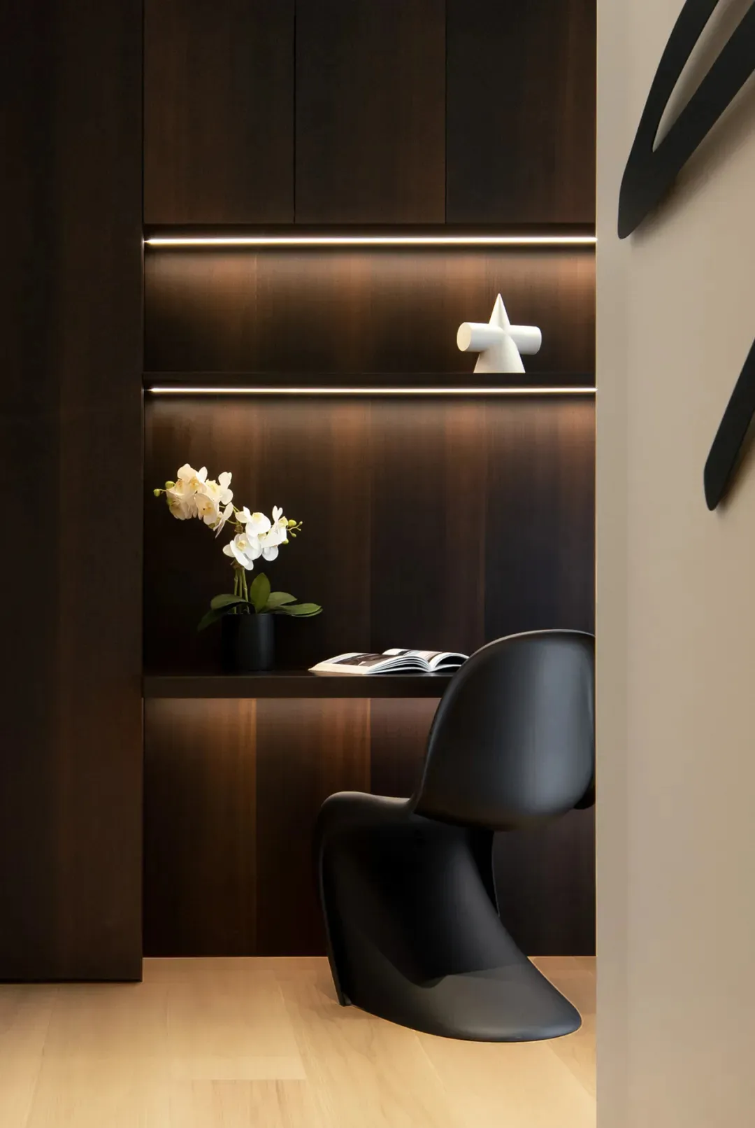 A modern minimalist office workstation with dark wood paneling and illuminated shelves.