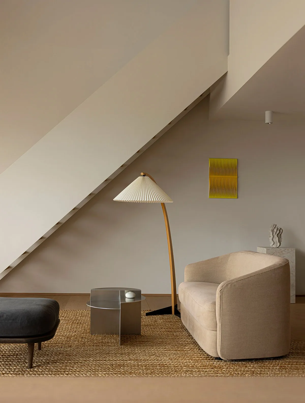 A modern living room with a grey sofa, a tall white pleated lamp, and a woven rug.