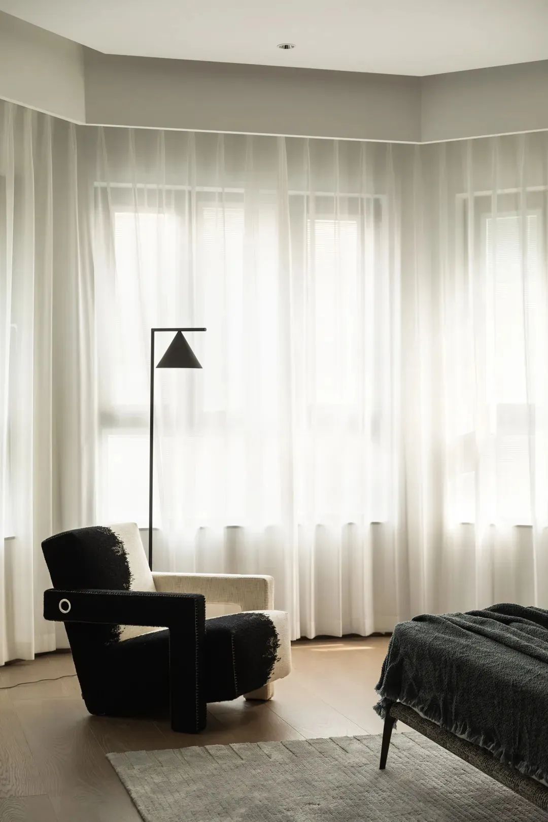 A modern bedroom featuring sheer white curtains allowing natural light to filter through.