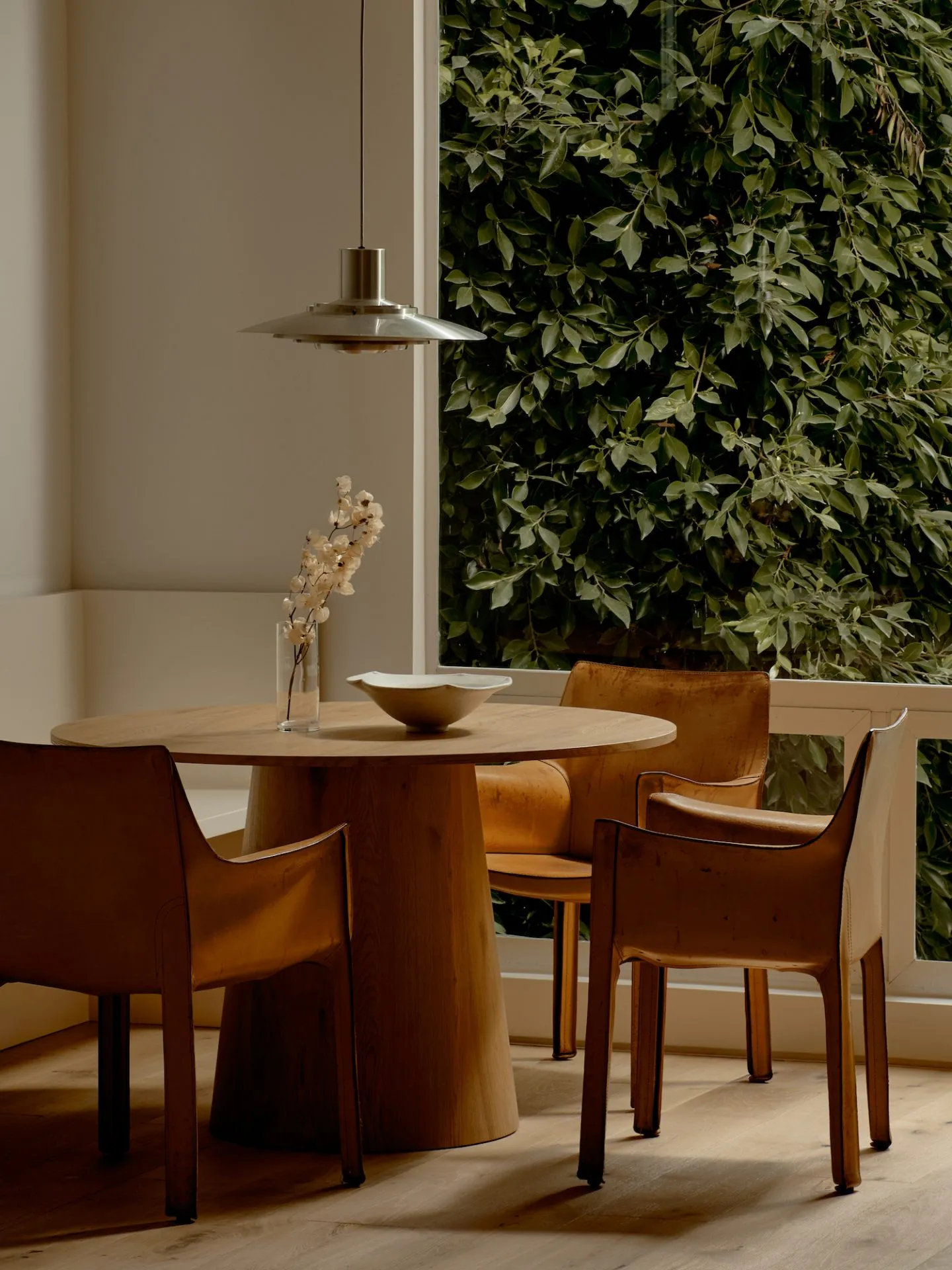 Modern dining room with a wooden table and leather chairs, featuring a vase of flowers and a bowl.