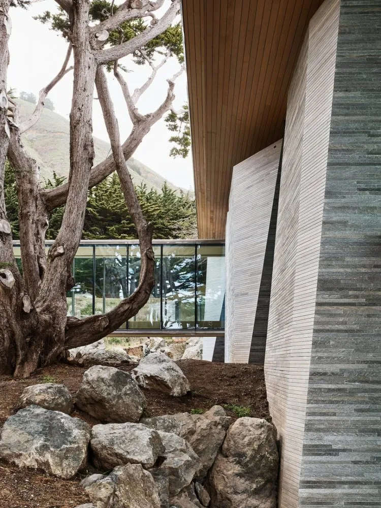 A modern wall composed of wood and stone materials, featuring a geometric design and a natural, rugged landscape in the backg