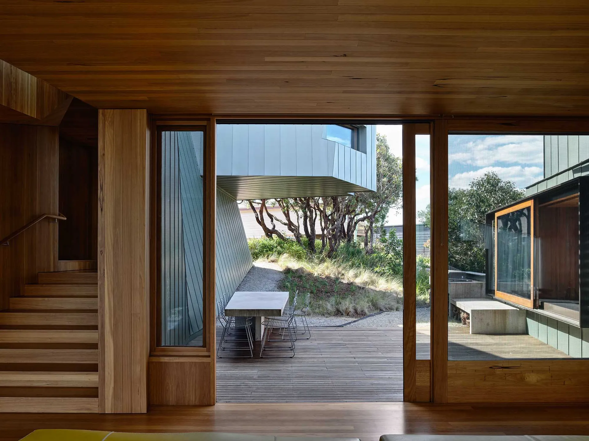 Modern interior design featuring wooden stairs and a wooden terrace with outdoor furniture.