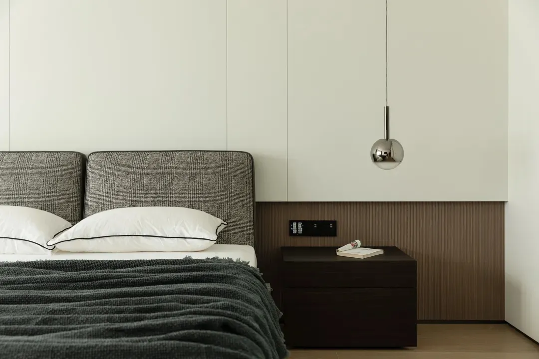 A minimalist bedroom with a fabric bed and metal pendant light.