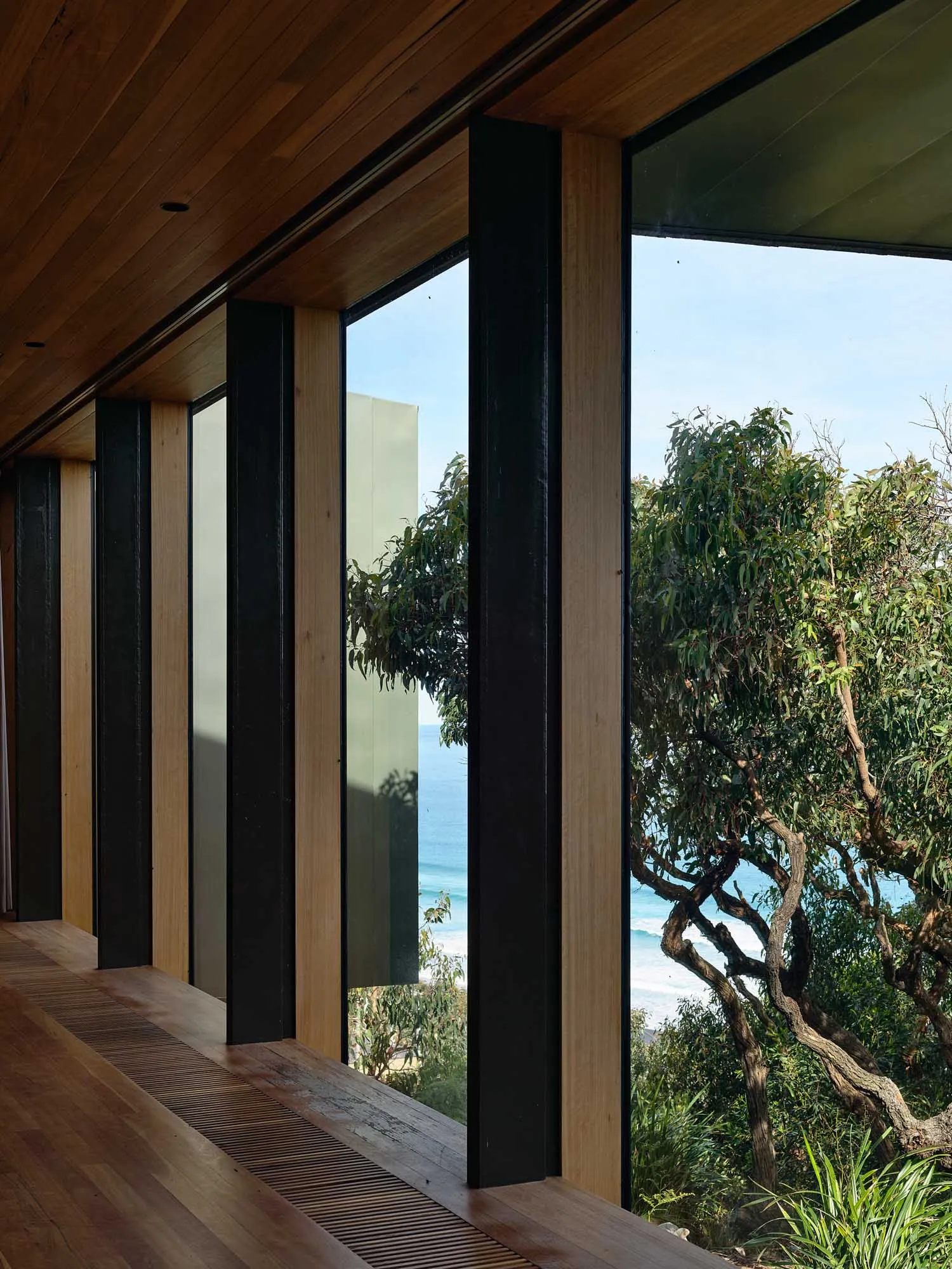 Modern residential interior with large windows overlooking the sea and lush greenery.