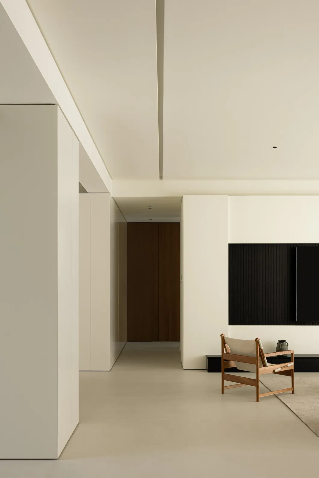 A minimalist living room featuring concrete walls and flooring, with a wooden chair and black television setup.